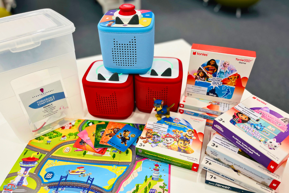 Auf dem Foto sind drei Tonieboxen 2 zu sehen. Auf einer der Boxen liegt eine Tonieplay Disc und der Tonieplay Controller auf. Vor den Boxen liegen ein Spielplan und Spielkarten aus einem der Tonieplay Games aus. Rechts neben den Boxen sind verschiedene Tonieplay Games gestapelt.