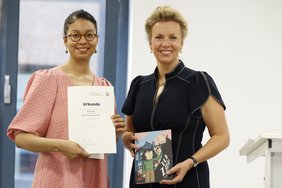 Das Bild zeigt die Ministerin und die Autorin mit dem Buch und der Auszeichnungsurkunde.