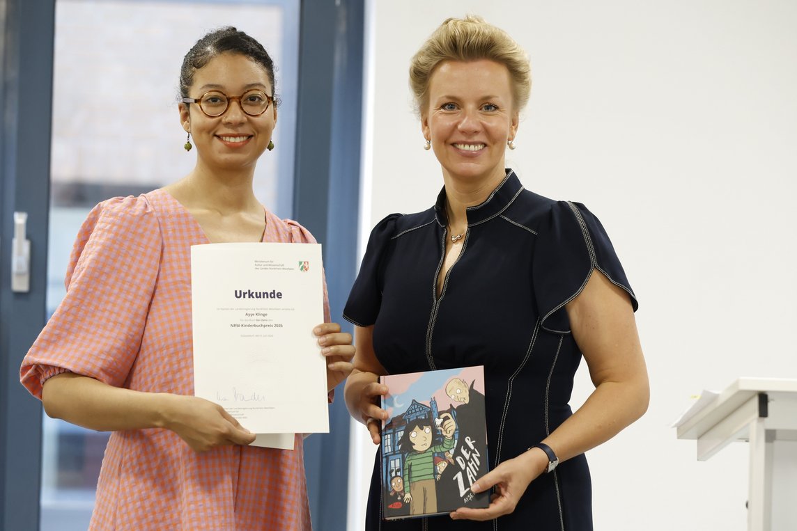 Das Bild zeigt die Ministerin und die Autorin mit dem Buch und der Auszeichnungsurkunde.