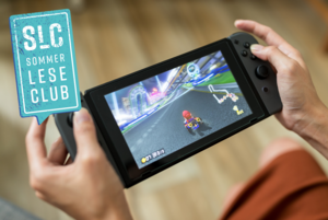 Auf dem Bild sieht man eine Nintendo Switch Konsole, auf der das Spiel Mario Kart läuft. Zwei Hände halten die Konsole.